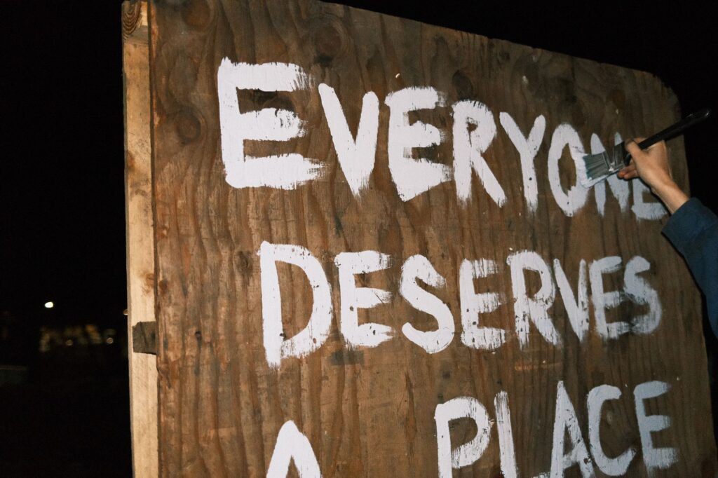 Hand painting "Everyone Deserves A Place" on a board with white paint. Photo by Elliot Patterson of Asheville Free Press