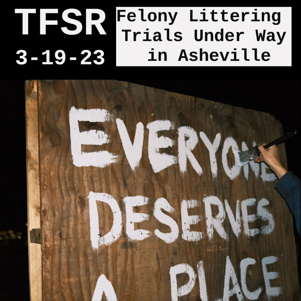 Hand painting "Everyone Deserves A Place" on a board with white paint. Photo by Elliot Patterson of Asheville Free Press framed by "TFSR 3-19-23, Felony Littering Trails Under Way in Asheville"